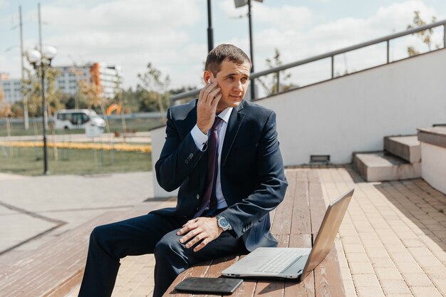 Een man in een pak en een laptop zit op een bankje. zakenman met laptop.