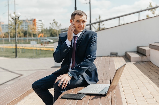 Een man in een pak en een laptop zit op een bankje. zakenman met laptop.