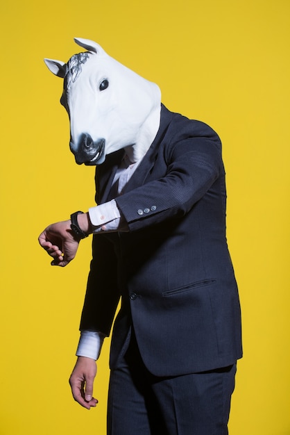 Een man in een pak en een paardenmasker die op zijn horloge kijkt Conceptuele zakelijke achtergrond