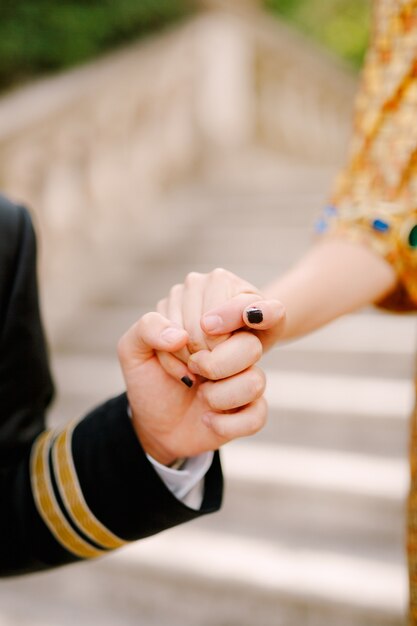 Een man in een pak en een vrouw in een gouden jurk houden elkaars hand teder vast