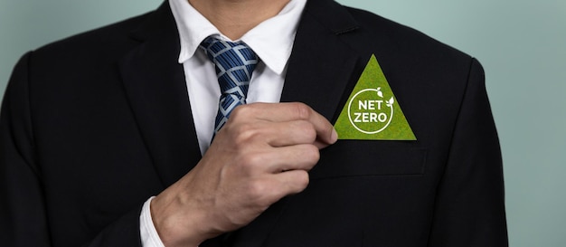 Foto een man in een pak houdt een groene driehoek vast met het net zero-logo erop.