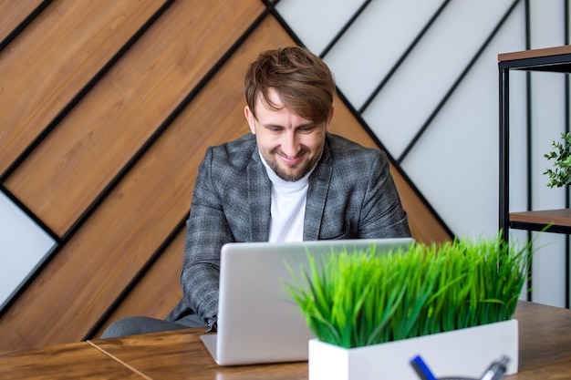 Een man in een pak zit op zijn werkplek naar een laptop te kijken en te lachen