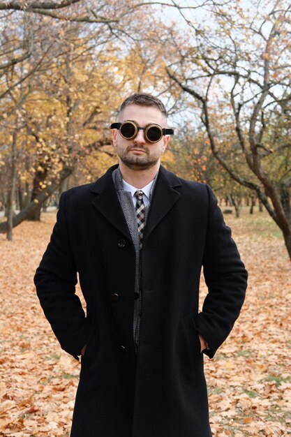 Een man in een pakjas en steampunk-bril poseert in een herfstpark Verticale foto