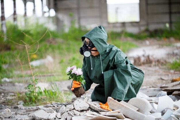 Een man in een regenjas en een gasmasker verzamelt een bloem van een verschroeid giftig land Luchtvervuilingsconcept Ecologische catastrofe