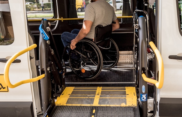 Een man in een rolstoel op een lift van een voertuig voor mensen met een handicap.