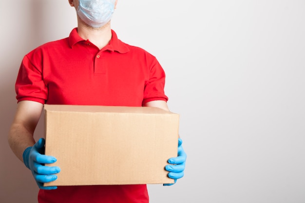 Een man in een rood uniform met een medisch masker en wegwerphandschoenen bezorgt