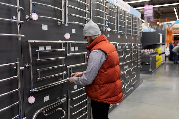 Een man in een sanitairwinkel kiest een metalen verwarmd handdoekenrek in de doucheruimte