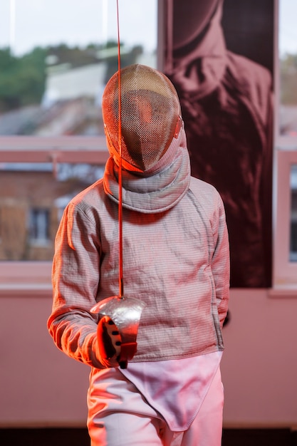 Een man in een schermpak met een zwaard in zijn hand, neonlicht. Een jong model traint en traint in beweging, actie. Sport, jeugd, gezonde levensstijl.