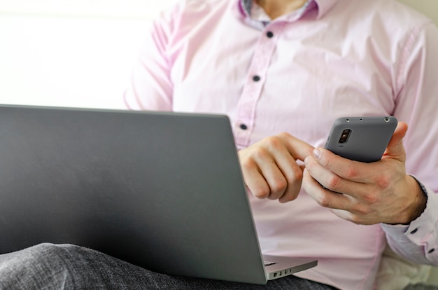 Een man in een shirt en spijkerbroek werkt op laptop en telefoon