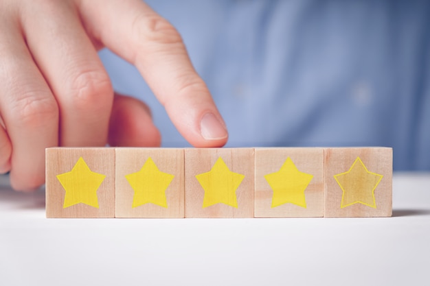 Foto een man in een shirt toont abstract de waardering met een vinger vier sterren op houten kubussen. goed cijfer