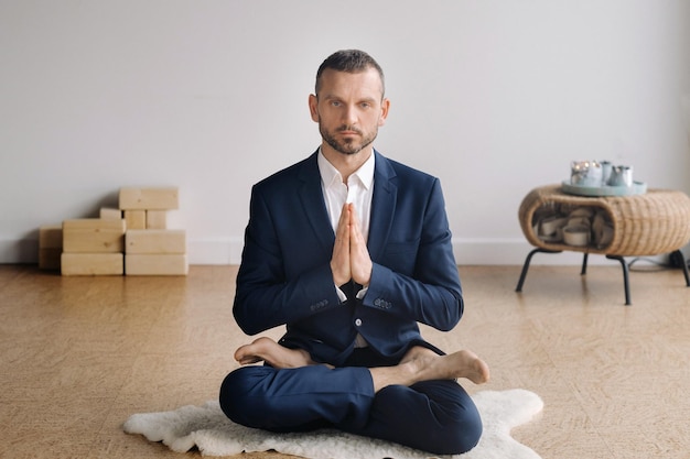 Een man in een strak pak doet yoga terwijl hij in een fitnessruimte zit