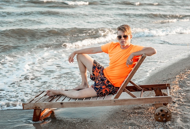 Een man in een T-shirt en korte broek zit op een ligstoel aan zee