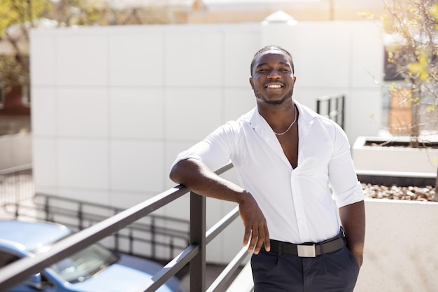Een man in een wit overhemd staat op een balkon en glimlacht.