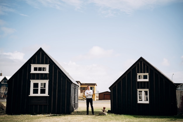 Een man in een wit overhemd tussen twee houten zwarte huizen bestemming ijsland bruiloft