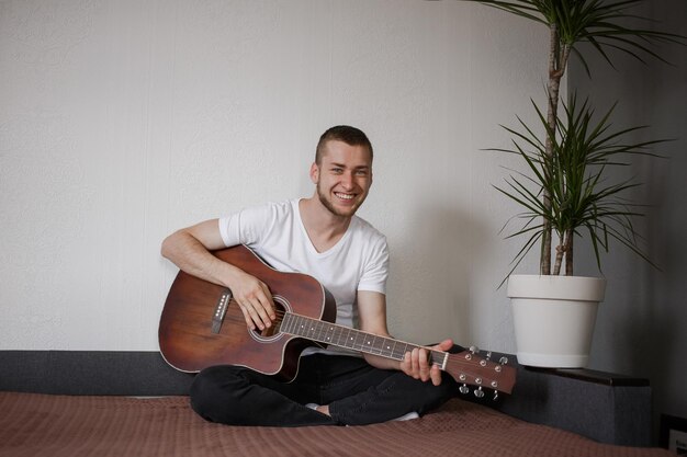 Een man in een wit T-shirt die gitaar speelt bij homexA