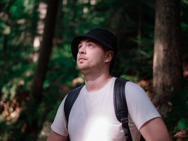 Een man in een wit t-shirt en een hoed kijkt op tegen een bosachtergrond