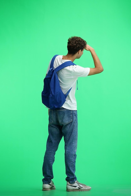 Een man in een wit T-shirt op een groene achtergrond met een rugzak kijkt in de verte