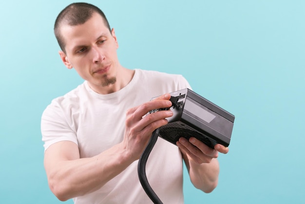 Een man in een witte t-shirt die een pin-kabel aansluit op een computervoeding op een blauwe achtergrond