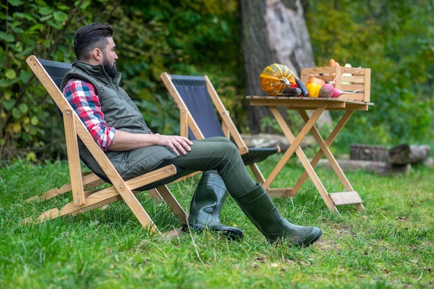 Een man in geruit hemd en vest zit in de tuin