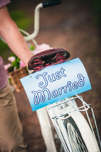 Een man in geruit overhemd houdt een fiets vast met een mand met bloemen en een inscriptie in het park