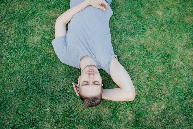 Een man in grijs T-shirt liggend op groen gras, zomer. Rustende man