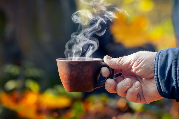 Een man in het herfstbos houdt een kop hete koffie vast, waaruit stoom komt