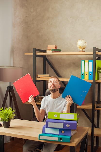 Een man in het kantoor achter een stapel mappen en een laptop.