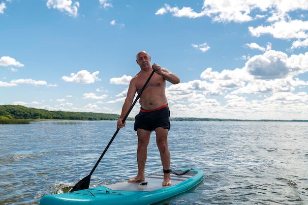 Foto een man in korte broek en een t-shirt op een sup-board in een meer op een zonnige dag tegen een hemel met wolken