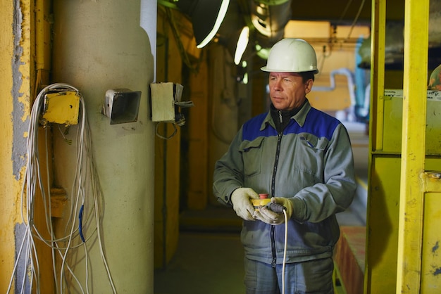 Een man in overall en een helm met een afstandsbediening op de werkplek