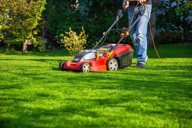 een man in spijkerbroek maait het gras in de tuin met een grasmaaier zomerdag