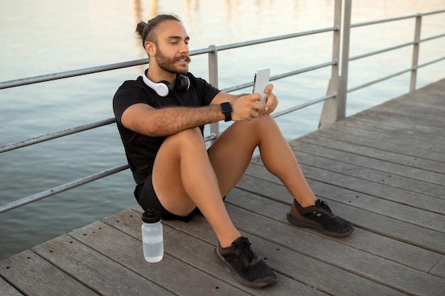 Een man in sportkleding kijkt buiten naar fitness-apps op zijn smartphone.