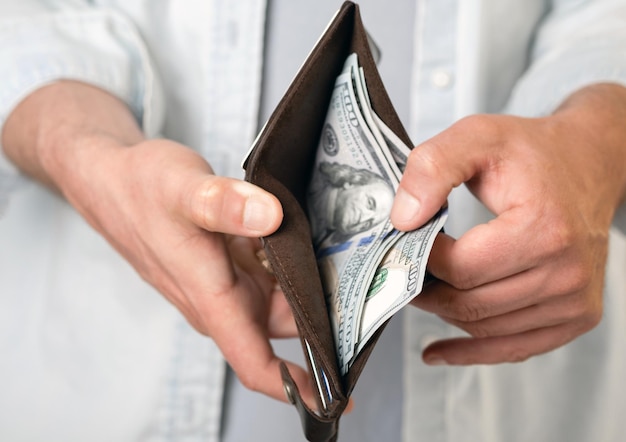 Een man in vrijetijdskleding heeft een mannelijke portemonnee met geld en honderd-dollarbiljetten in zijn handen