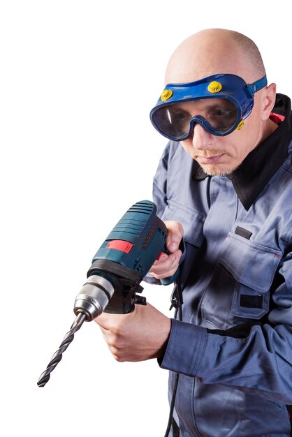 Een man in werkkleding in bril met een elektrische boor