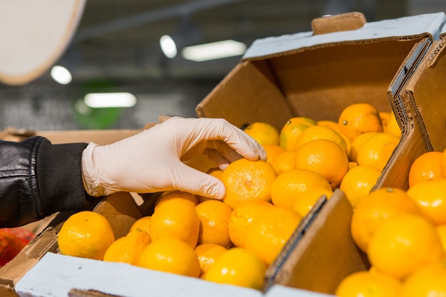Een man in witte handschoenen in een winkel koopt voedsel. man houdt een sinaasappel in zijn handen