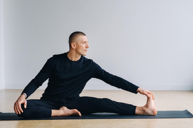 Een man in zwarte sportkleding doet yoga stretching in de sportschool