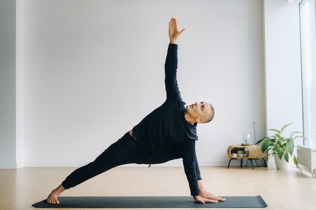 Een man in zwarte sportkleding doet yoga stretching in de sportschool