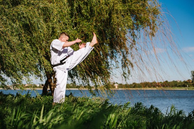 Een man karate vechter in witte kimono training buiten in het park