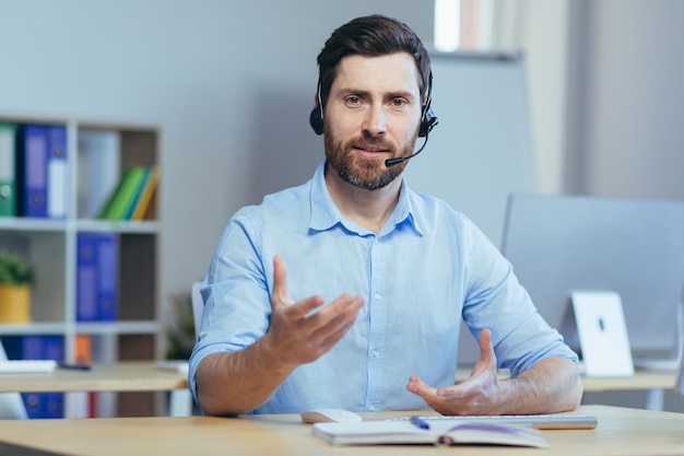 Een man kijkt naar de camera en praat tijdens een videogesprek met een headset een zakenman werkt in een licht kantoor