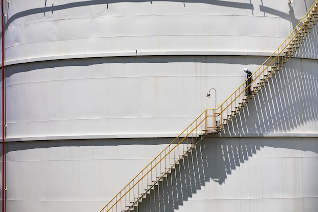 Een man loopt boven de inspectie-opname van de olietrap van de opslagtank op de zijkant van de schaalplaat