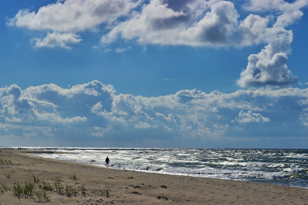 Een man loopt langs de kust van de zee tegen de achtergrond van golven