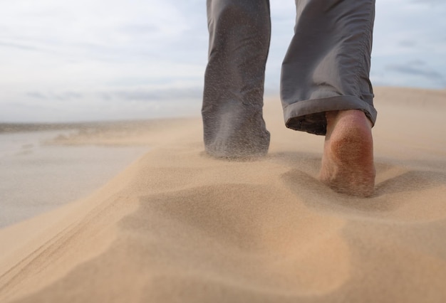 Een man loopt langs het zandstrand In de lucht vliegen zandkorrels van een sterke wind