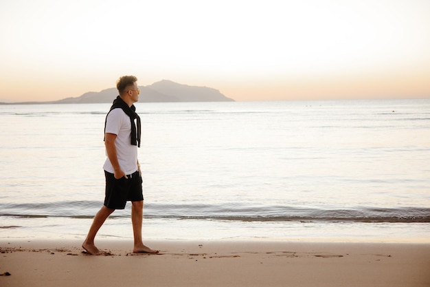 Een man loopt op het strand voor een zonsondergang.