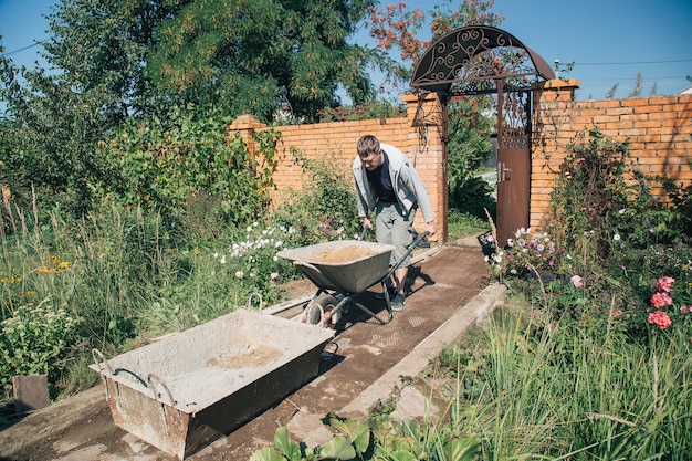 Een man lost zand in een cementmengsel voor het gieten van een tuinpad, bouwwerkzaamheden op een tuinperceel