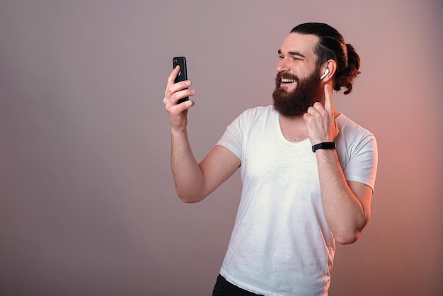 Een man luistert naar de muziek die in de telefoon kijkt en de oorschelp aanraakt