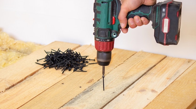 Een man maakt reparaties in het huis, een schroevendraaier, schroeven, een zaag. Houten vloer. Selectieve focus