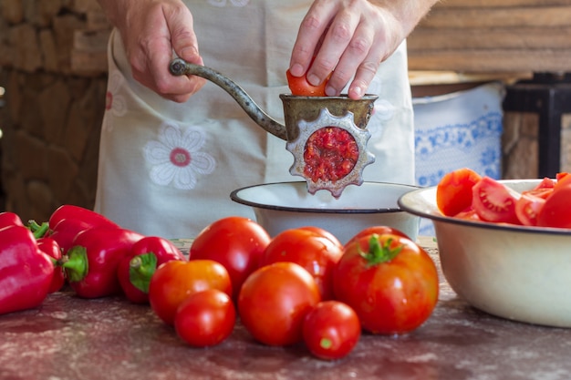Een man maalt tomaten en paprika&#39;s in een vleesmolen om Lecho-saus te bereiden