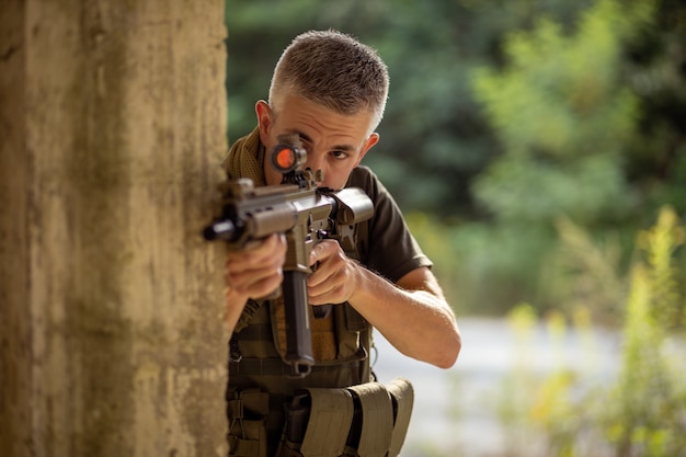 Een man met een airsoft aanvalsgeweer in militair uniform achter dekking