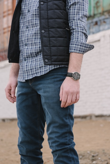 Een man met een baard en zonnebril in een geruite overhemd en vest poseren op straat