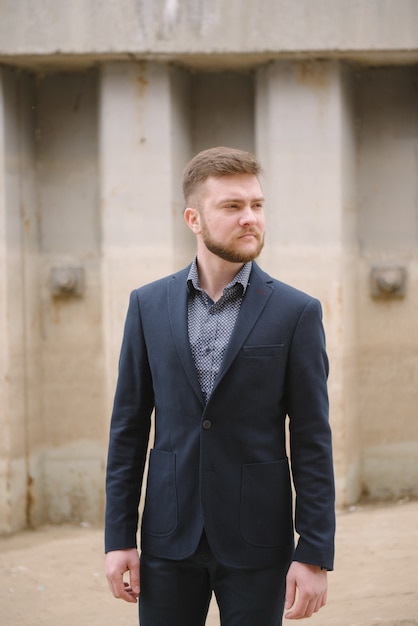 Een man met een baard in een blauw pak poseert op straat om reclame te maken voor herenkleding.