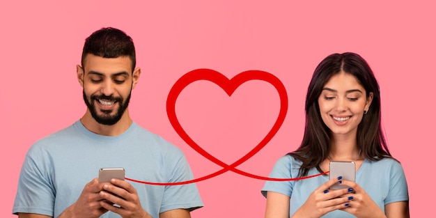 Een man met een baard in een blauw T-shirt glimlacht naar zijn telefoon terwijl een vrouw met lang haar in een soortgelijk